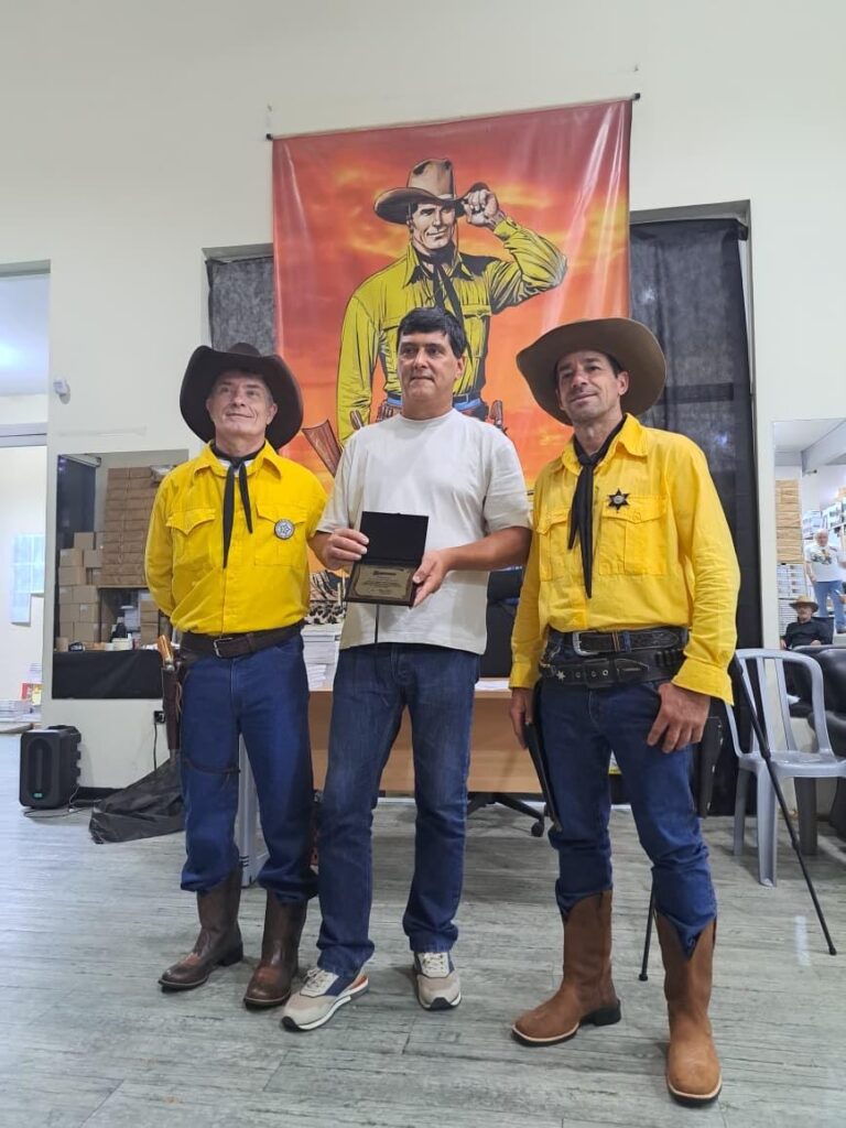 Outro momento repleto de emoção na Mythos Editora quando Delair Turella e João Marin entregam a placa de homenagem da Comissão do EnconTex 2026 a José Carlos Francisco
